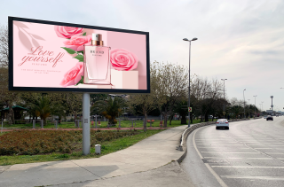 A large billboard on a roadside displays a perfume ad with pink roses and a perfume bottle on a pink background. Text reads "Love yourself."